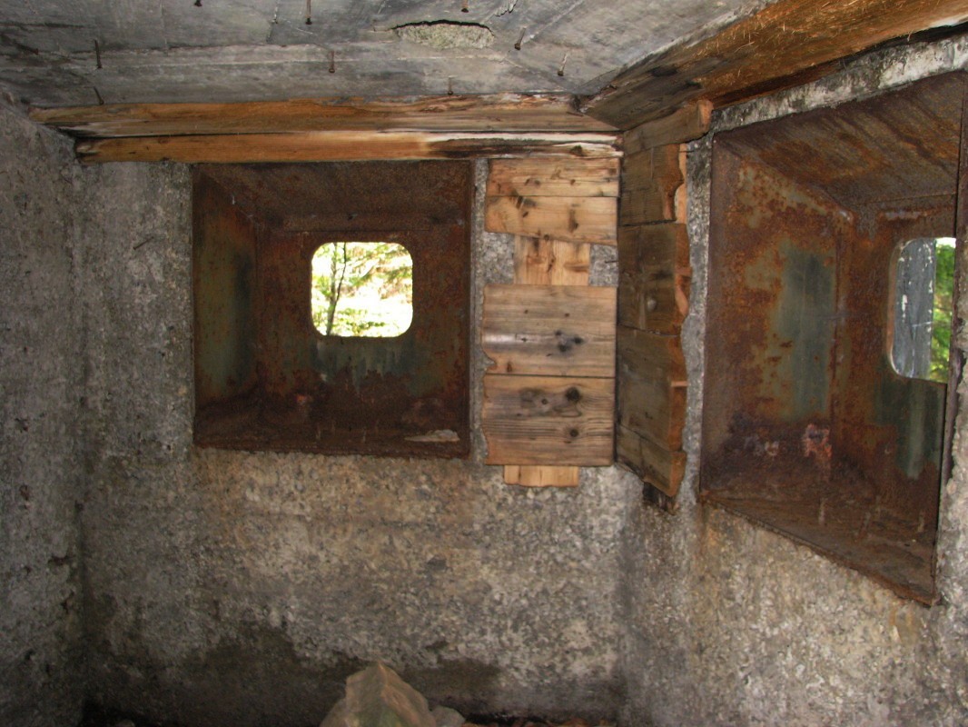 V notranjosti s pogledom na strelne line vojaškega bunkerja na zahodnem in poraščenem pobočju gozdnega vrha Žbont (1295 m)