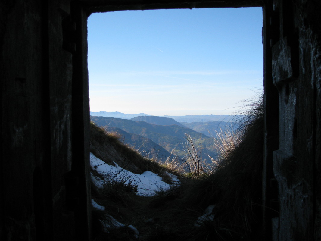 Pogled na gozdni, po grebenu razgledni vrh Kojco (1303 m) nad vasico Zakojca (706 m) in Hudajužno, skozi vhod v podzemne labirinte, v ospredju dolgi gozdni greben vzhodno proti Poreznu (1630 m)